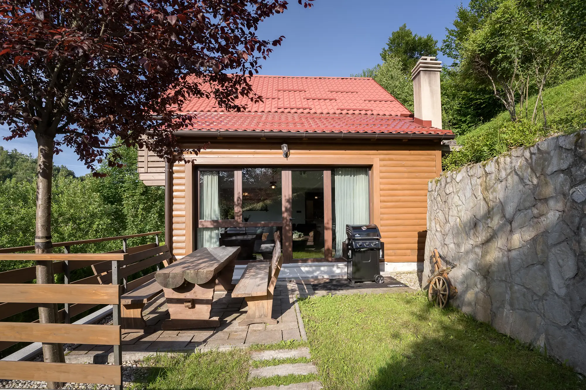 Drvena terasa s roštiljem, stolom s klupom od trupaca i staklenim kliznim vratima